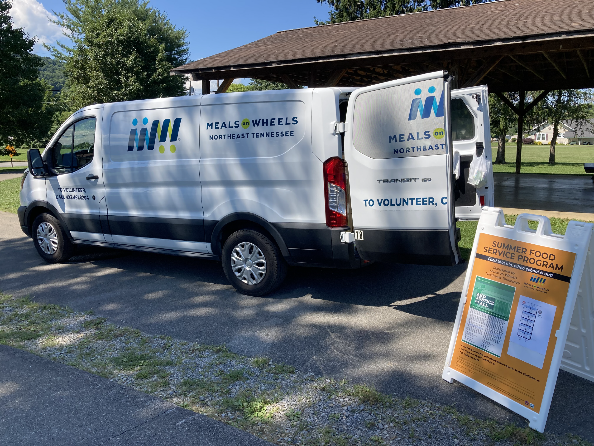 A Meals on Wheels van's trunk open with Summer Food boxes in the back.
